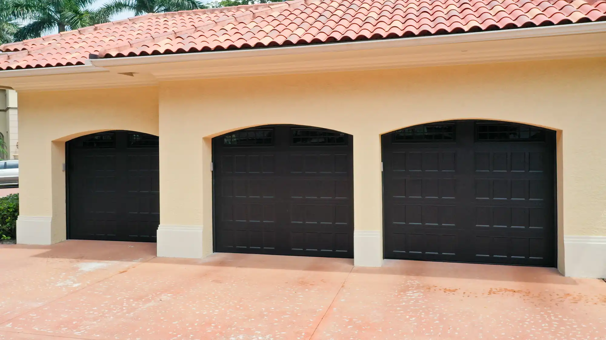 Completed installation of three black garage doors with decorative windows in a beige residential building.