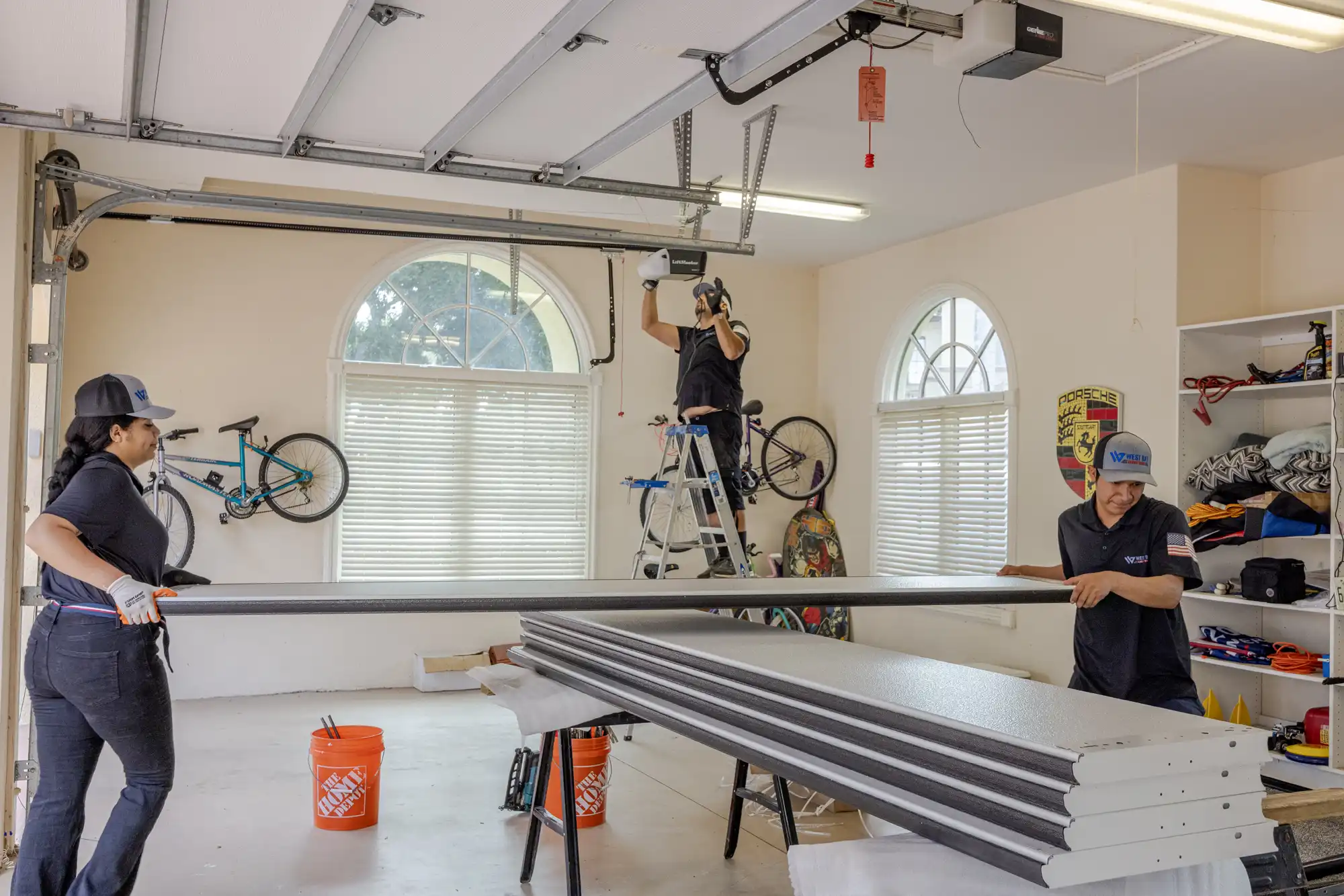 Three technicians collaborating on a garage door installation inside a residential garage, using ladders and tools.