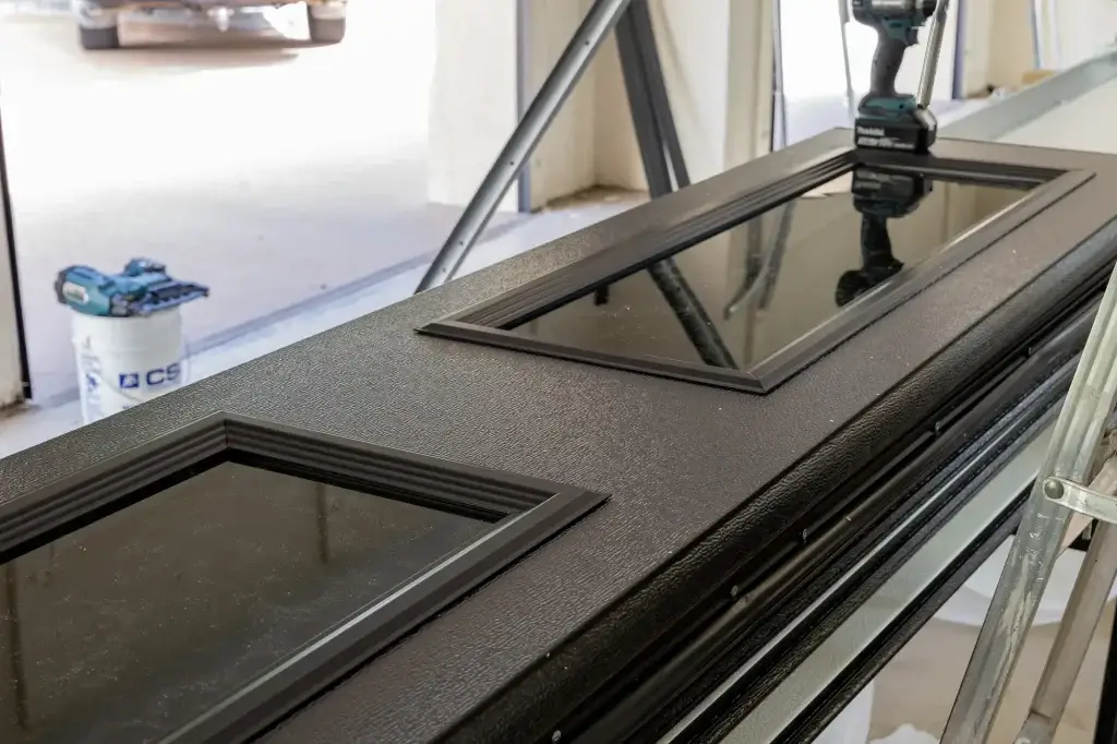 ose-up of a black garage door panel with decorative glass inserts placed on a workbench during installation."