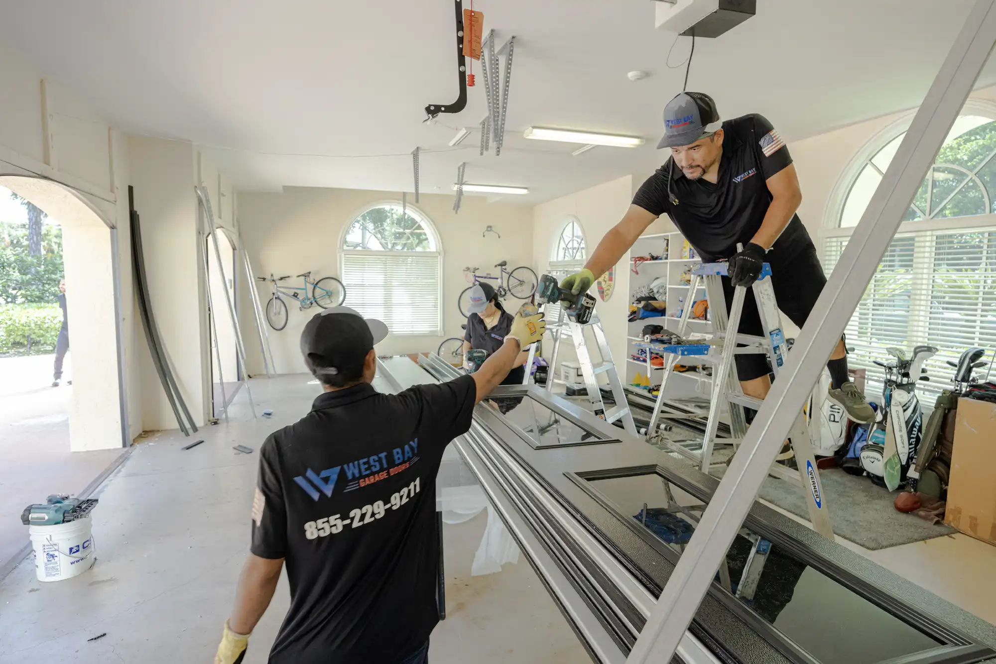 Two men in West Bay Garage uniforms passing drill to install garage opener