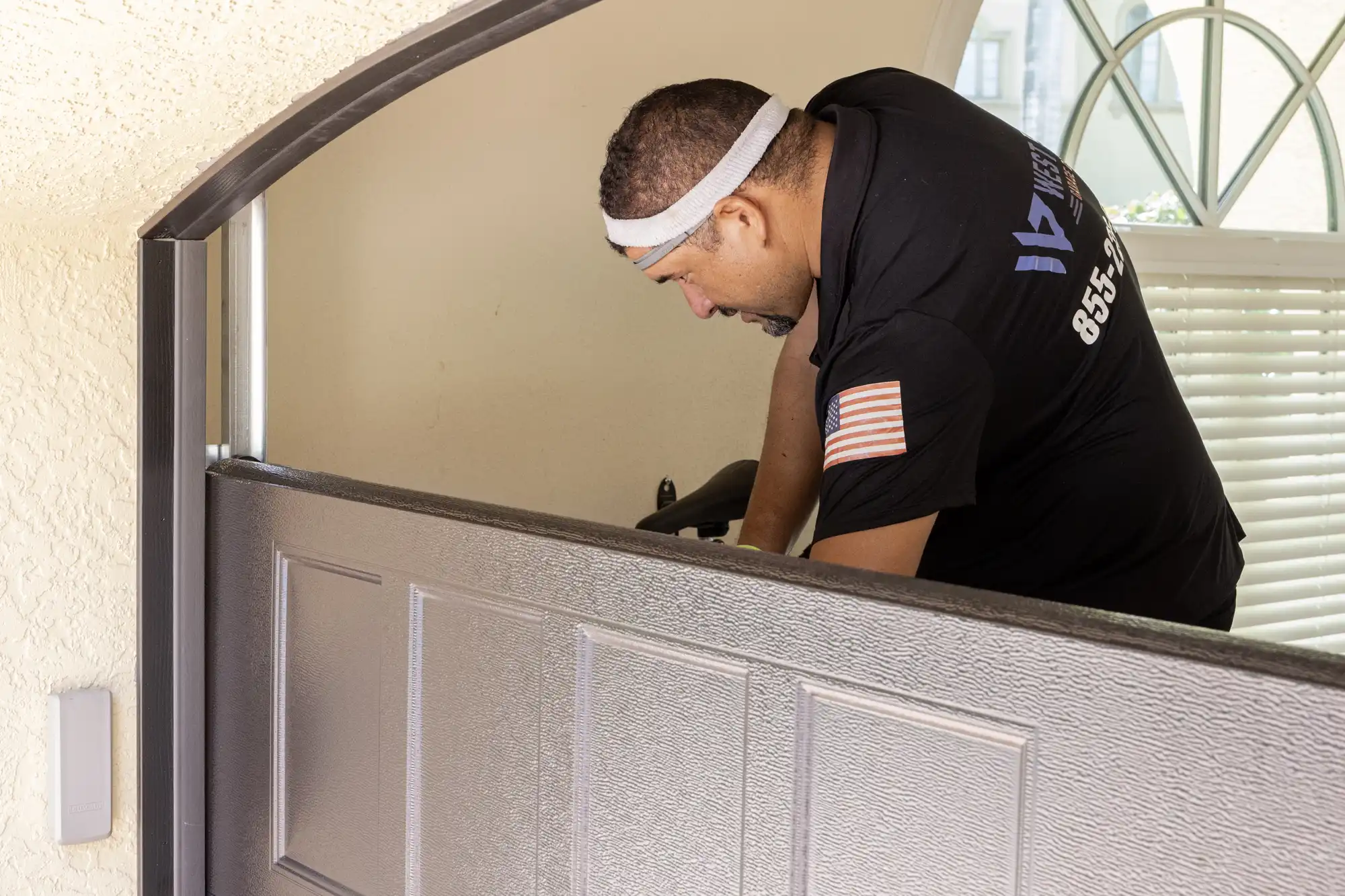 Technician installing or repairing a garage door, focused on their work, wearing a black uniform with an American flag patch on the sleeve.