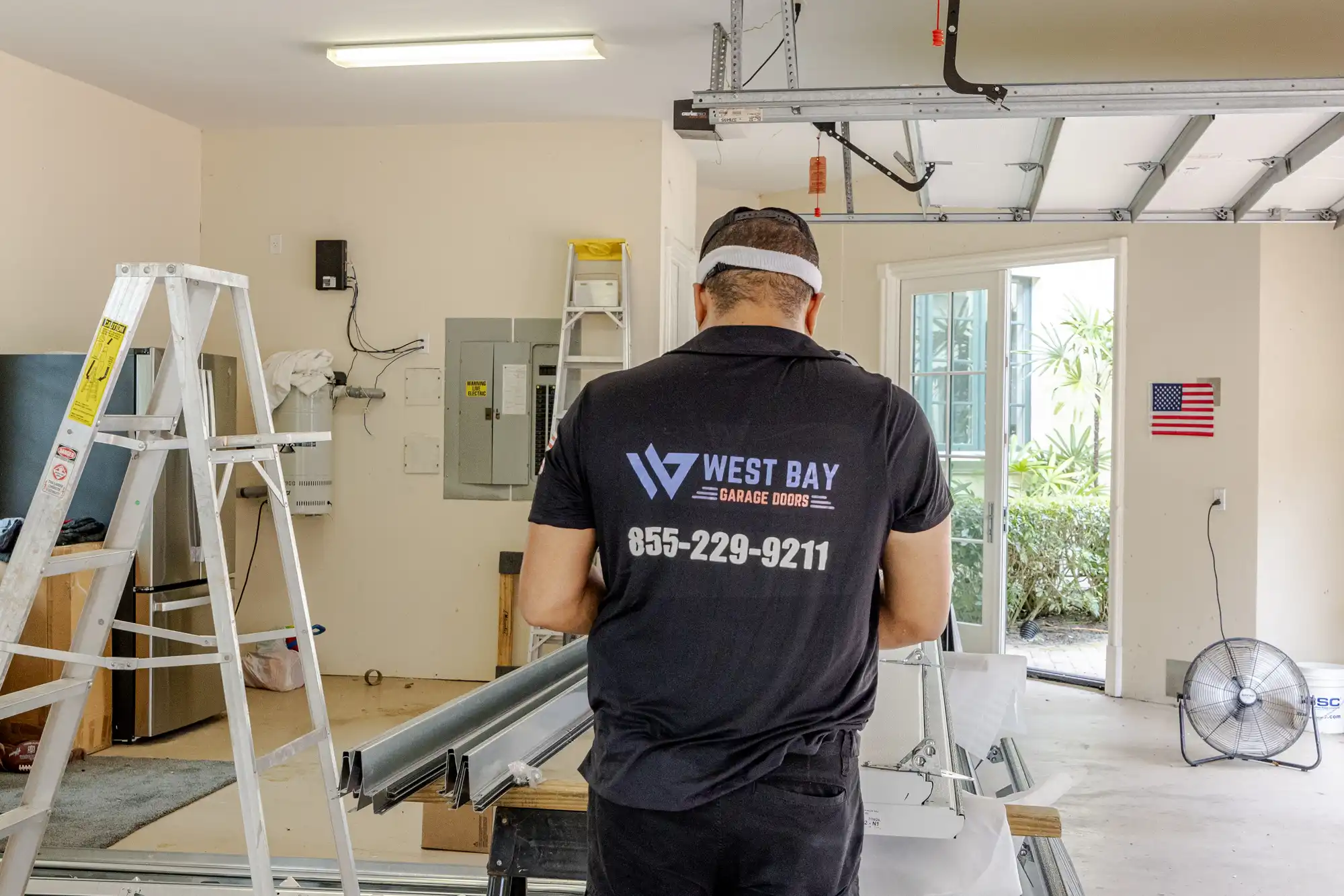 Technician wearing a black uniform with 'Falcon Level Garage Doors' branding, assembling garage door components in a residential garage.